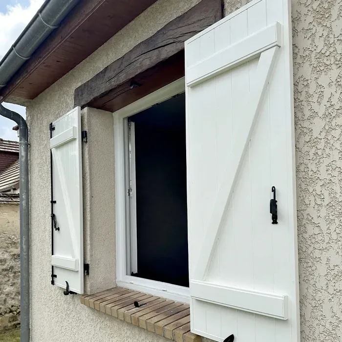Volet battant aluminium blanc ouvert contre la façade d'une maison traditionnelle en enduit gratté