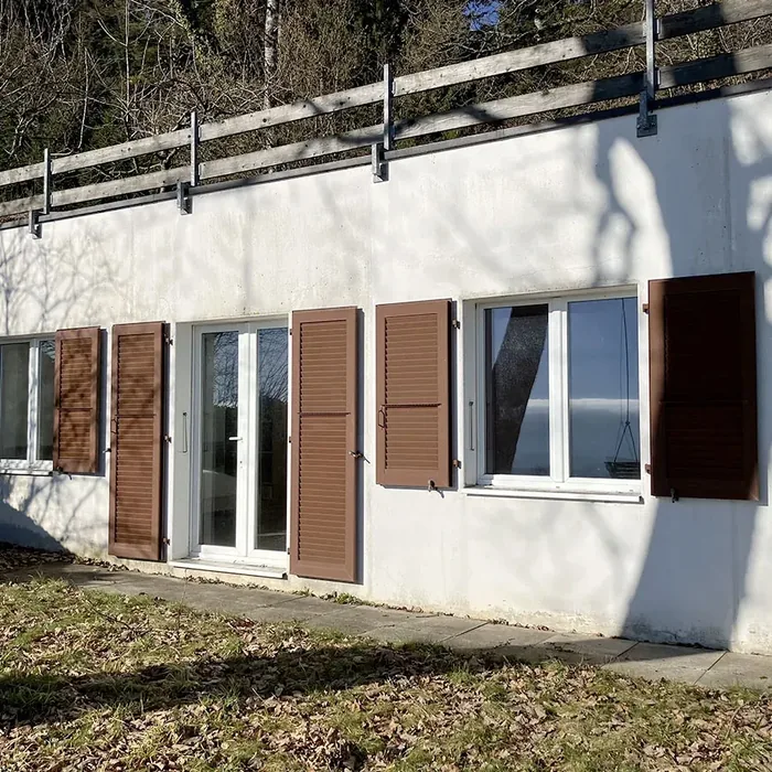 Volets battants persiennĂ©s marron en aluminium sur une façade blanche, fenĂȘtres et porte-fenĂȘtre