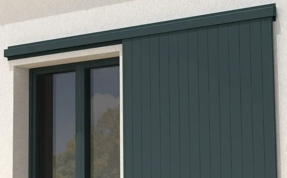 Volet coulissant aluminium vert foncé ouvert, garé sur le mur à droite d'une fenêtre, rail haut courant sur toute la façade
