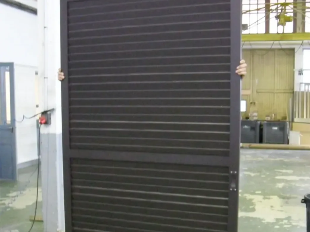 Grand vantail coulissant persienné en aluminium foncé, vérifié en atelier avant expédition