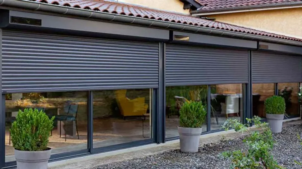 Quatre volets roulants solaires anthracite alignés au-dessus de baies vitrées sous un débord de toit