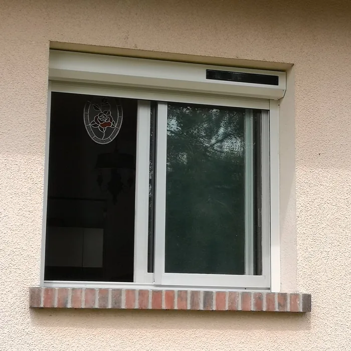 Volet roulant solaire blanc au-dessus d'une baie coulissante à appui de brique