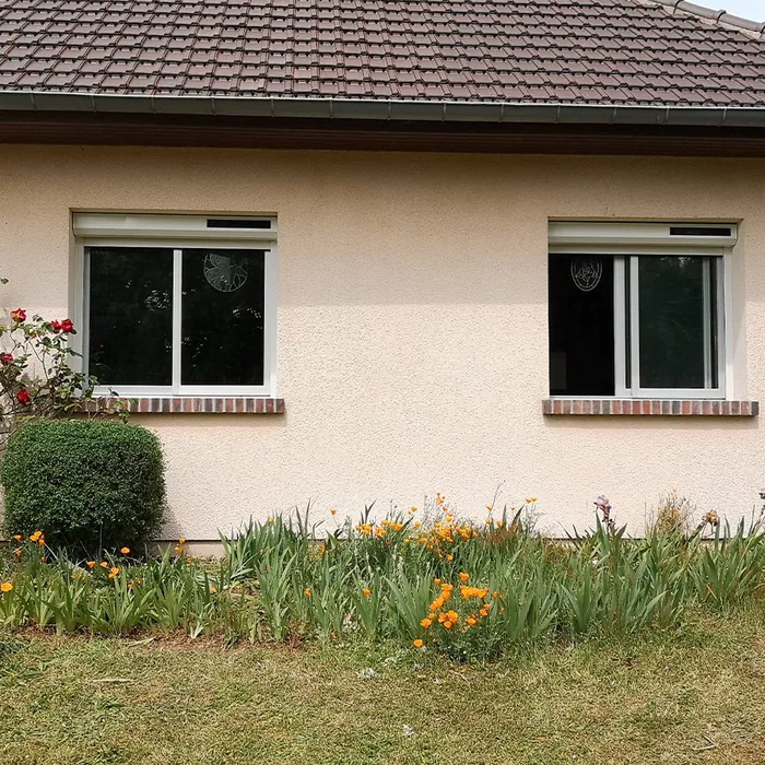Deux volets roulants solaires posés en rénovation sur la façade beige d'une maison de plain-pied
