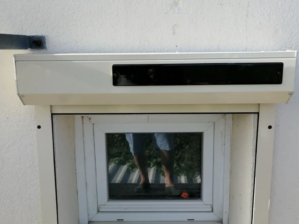 Volet roulant solaire blanc posé en applique sur la façade au-dessus d'une petite fenêtre